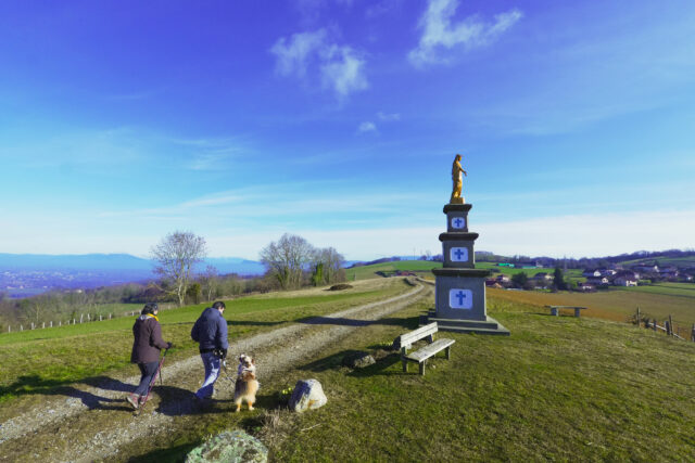 Couple et chien qui marchent près de la statue de la Madone à Valencogne
